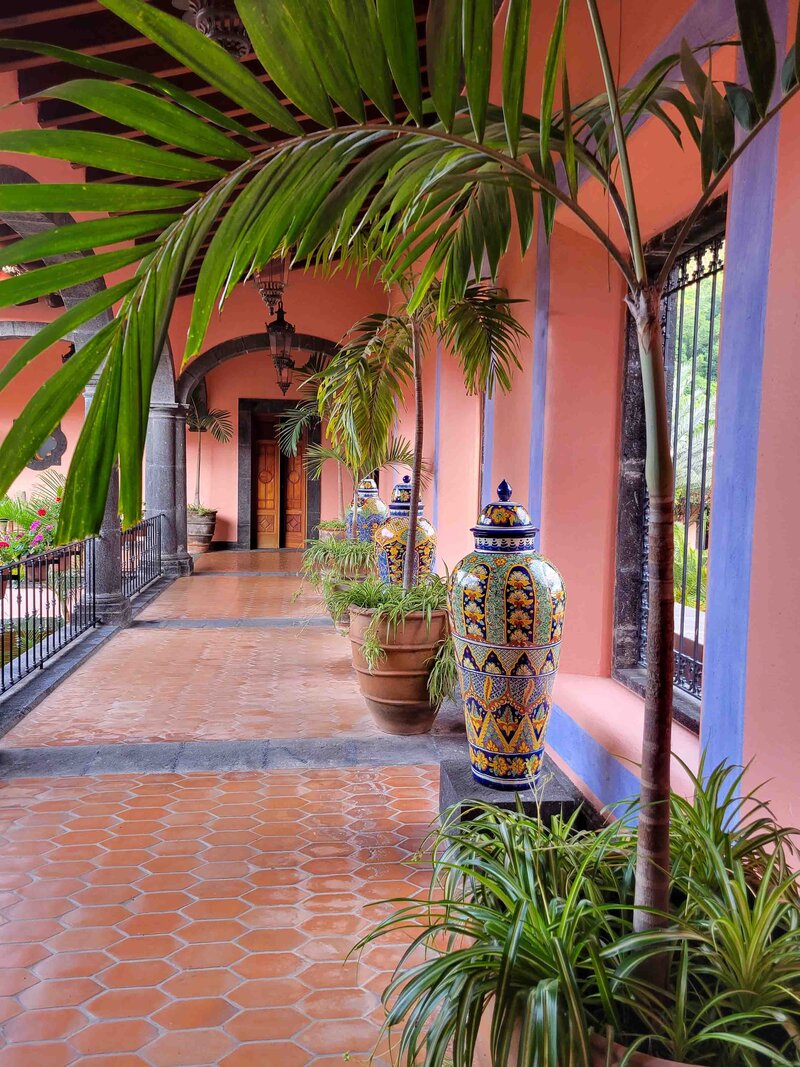 Terracotta-tiled corridor with palm trees and colorful Talavera vases at Hacienda de San Antonio, Colima, Mexico, an exquisite destination for luxury travelers seeking an elegant retreat ©Stephanie Dosch | theViatrix Luxury Travel