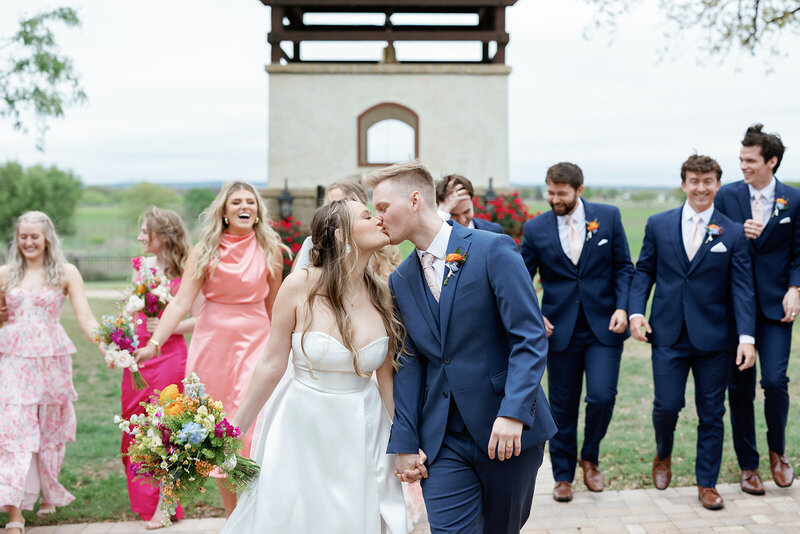 Bride and groom with their bridesmaids and groomsmen, dressed in pink spring dresses and suit attire with a Texas hill country background