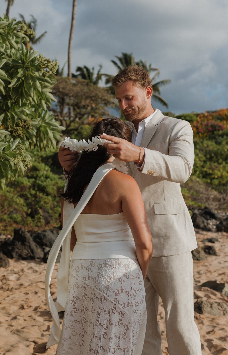 groom giving bride a lei on beach