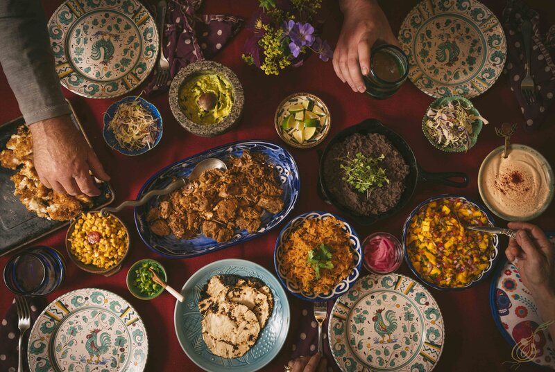 A vibrant table laden with various Mexican dishes, surrounded by people enjoying their meal together.