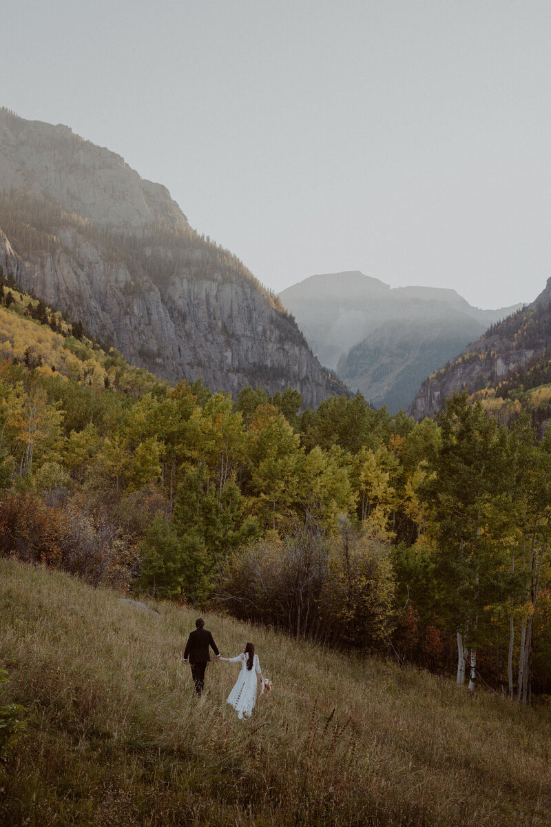 Bride and groom stand in a meadow in the mountains