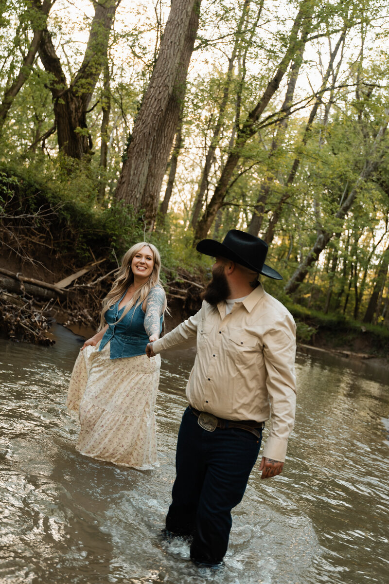 Couple sharing a tender moment near a creek, surrounded by nature’s tranquility, captured in a beautiful outdoor setting.