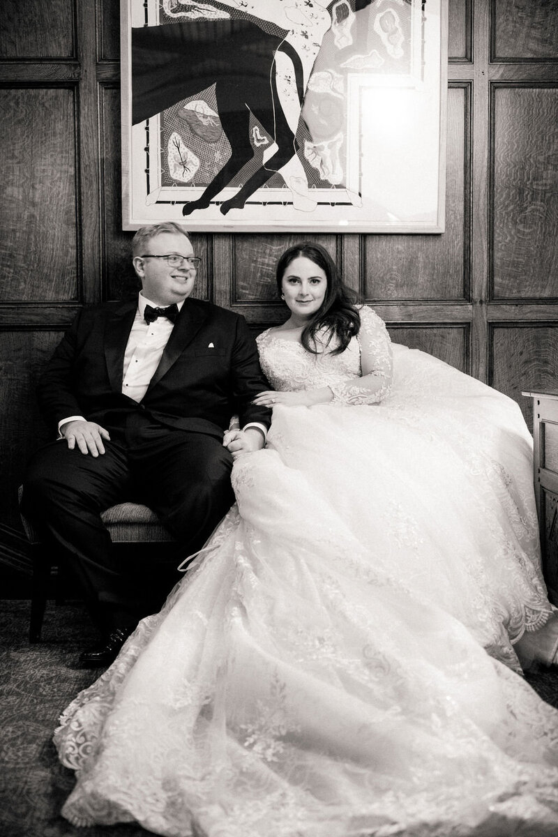 Bride in a lavish gown seated beside the groom on a vintage couch, under a stylish monochrome artwork.