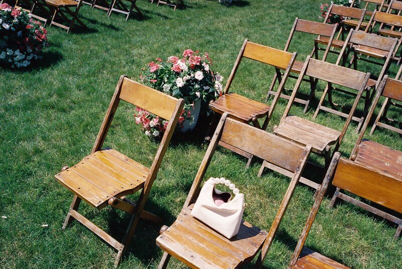 wooden seats on lawn for wedding ceremony with flowers framing aisle and small purse on one seat by photographer tom thornton in minnesota