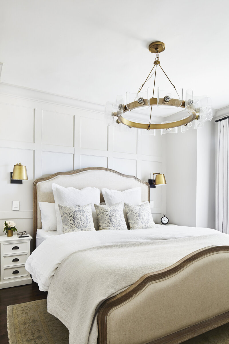 timeless luxury bedroom with wall panelling gold lighting upholstered linen and wood bed with vintage rug gold wall sconces and white nightstands designed by Lark & Linen interior design