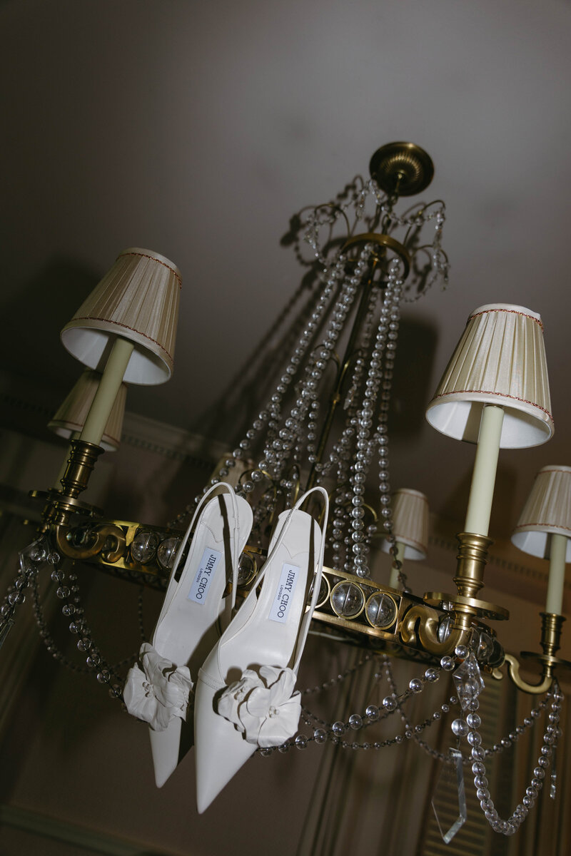 Elegant bridal heels displayed on a gold chandelier for editorial wedding detail shot by Clar Barron Photo.