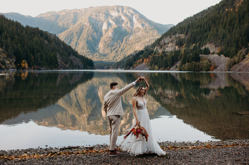 a couple at the shores of Diablo Lake in wedding outfits twirl together 