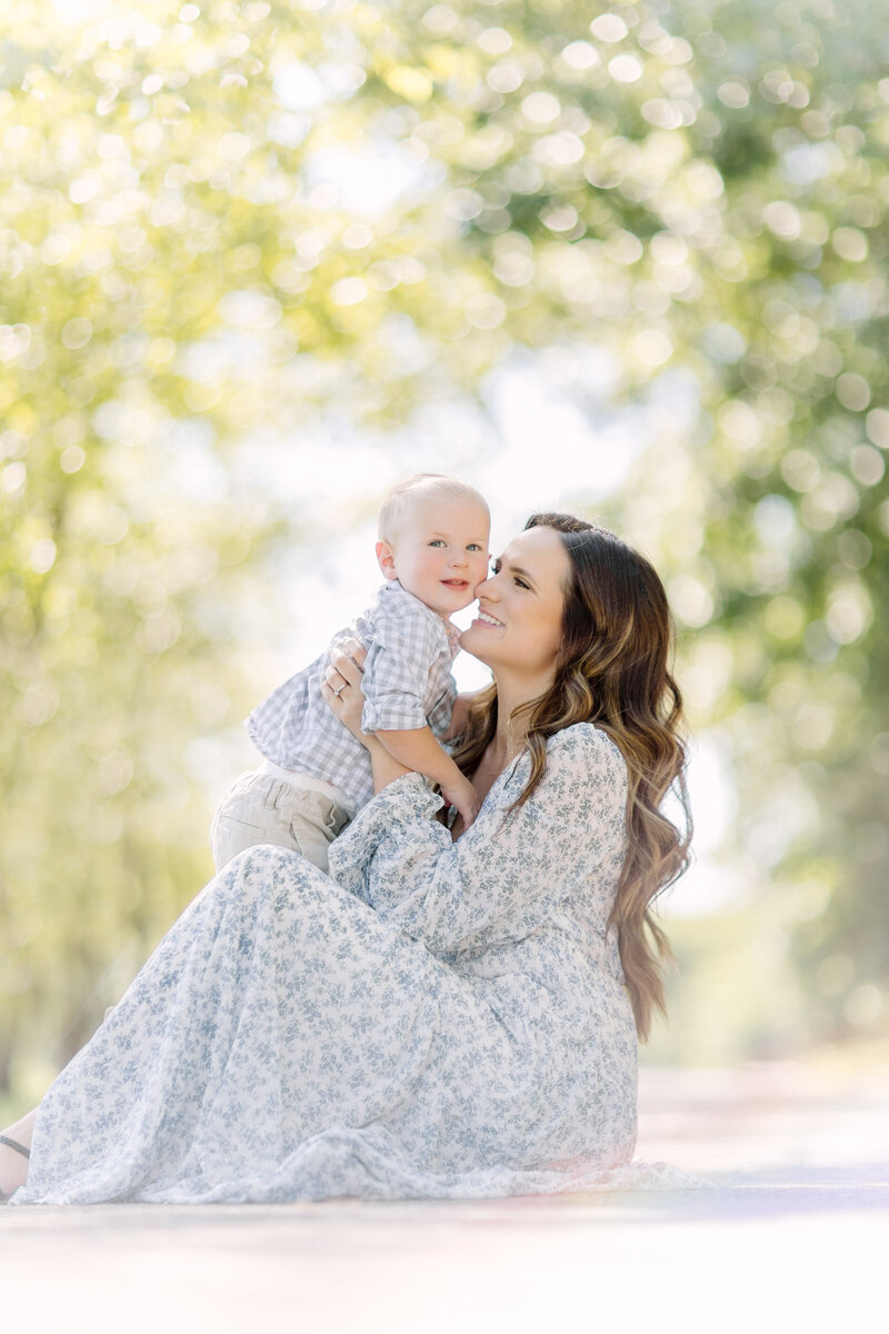 Mom in a light blue floral dress holding her young son next to a lake in her family photos by Kansas City photographer Jeanna Hayes