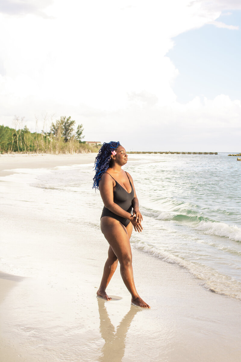 Model walks in surf wearing ecofriendly one piece black swimsuit