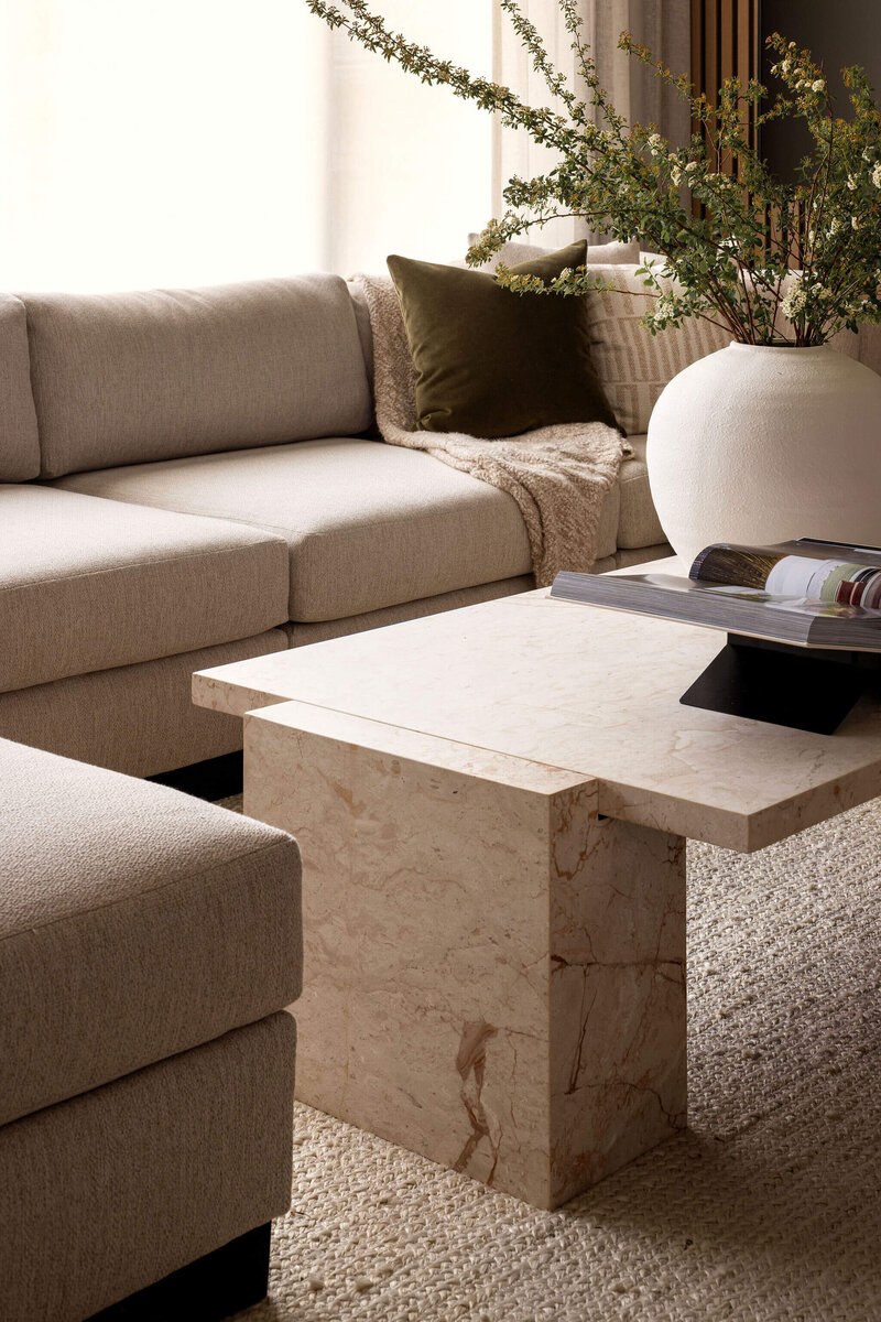 Japandi-style living room with natural marble coffee table, custom U-shaped sectional, and fresh greenery.