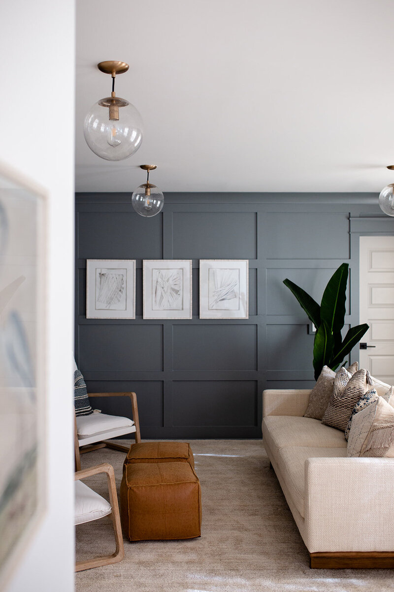 Dark blue tiled wall with minimalistic pictures. Couch and green plant provide contrast.