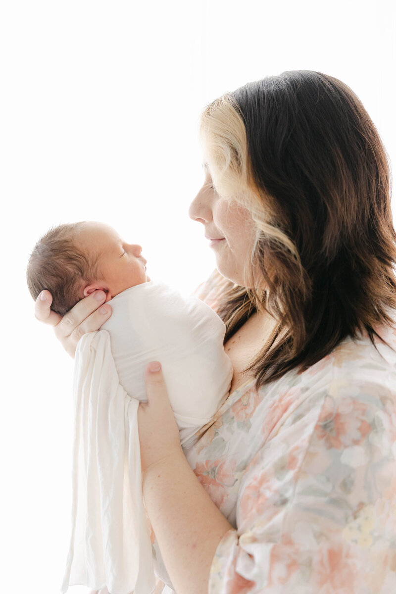 Mother holds her swaddled newborn while looking at his tiny face, Indianapolis photographer