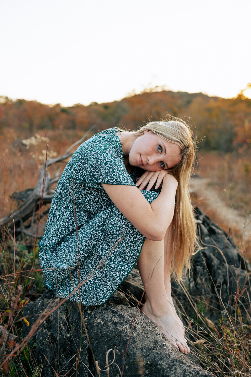 Senior girl sitting on a rock looking at a scenic location in De Soto, Missouri. 