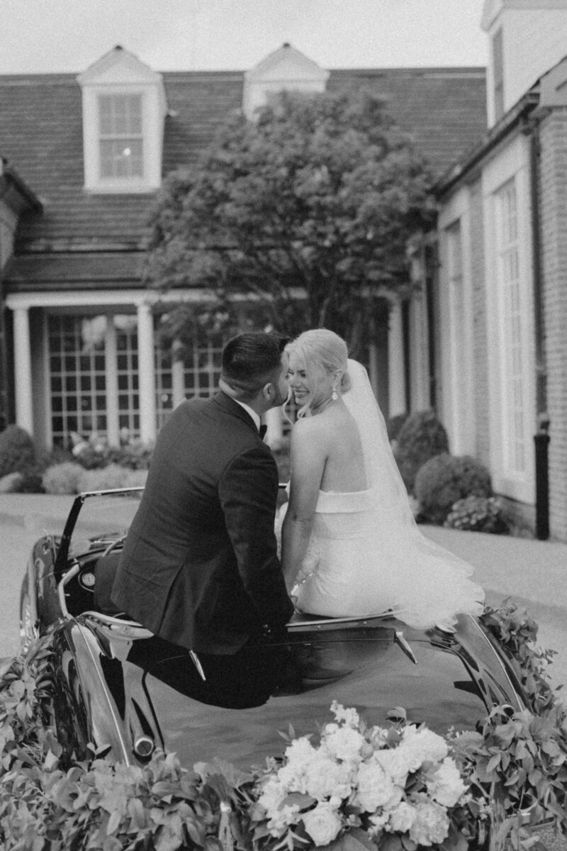 black and white photo of bride and groom about to kiss in a vintage car
