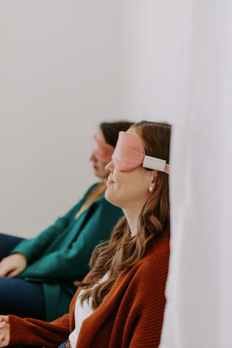 2 women wiht pink eye masks on sitting on floor subconscious reprogramming modalities