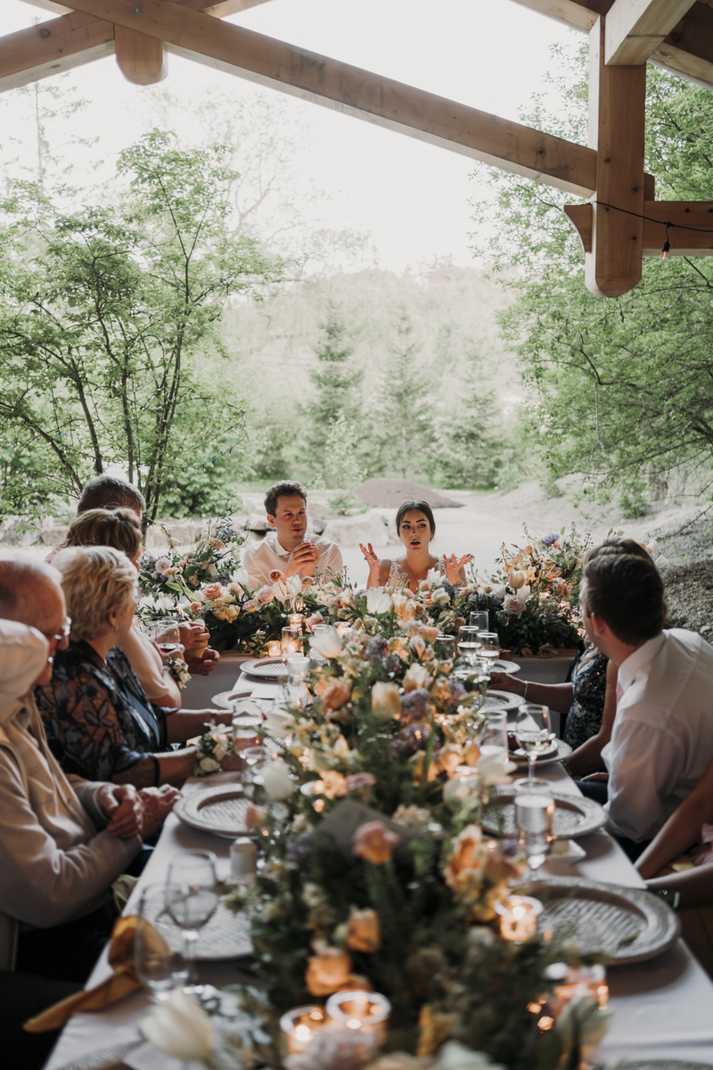 A long table with forest landscape in the background with bride and groom seated at the end with lush florals along the table