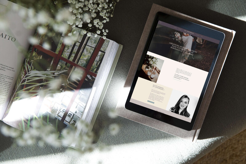 an ipad shows a wedding planner website in lovely muted colors, the table is on a grey couch and there are white flowers standing to the left side