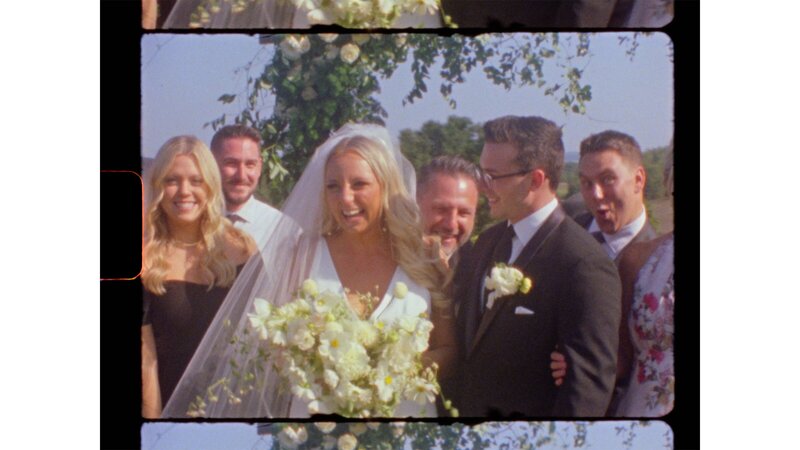 a bride and groom smile with friends and family and hold beautiful white flowers - a frame from a roll of Super 8 film