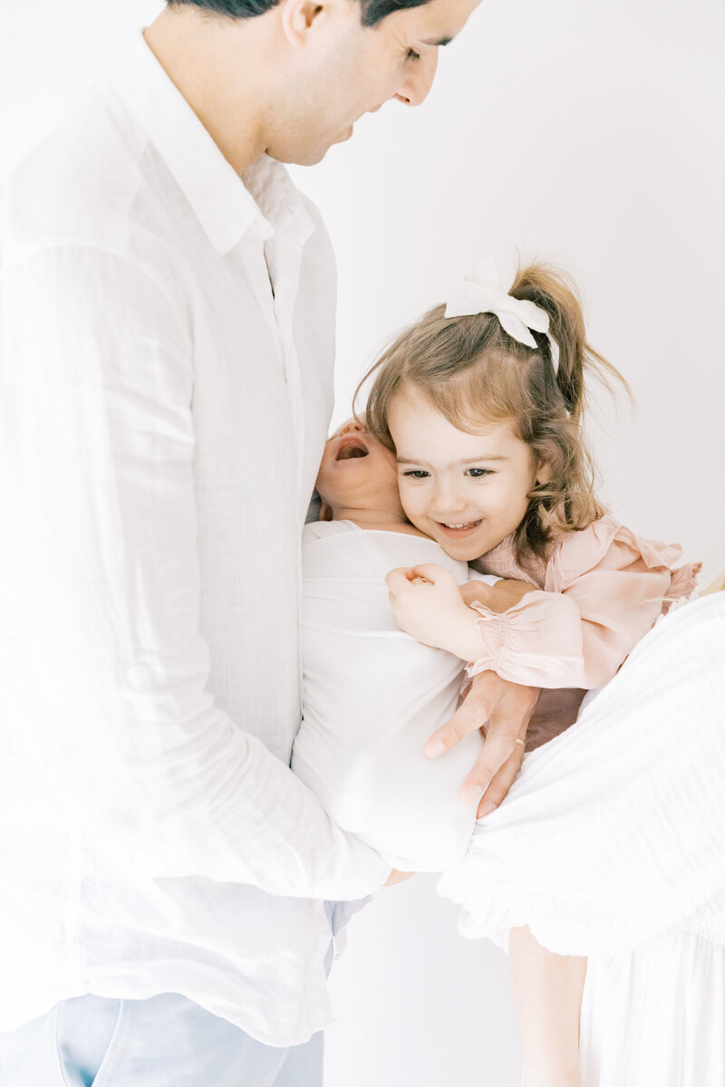 A toddler girl cuddles her newborn baby sibling in mom and dad's arms taken by a Charlotte Family Photographer