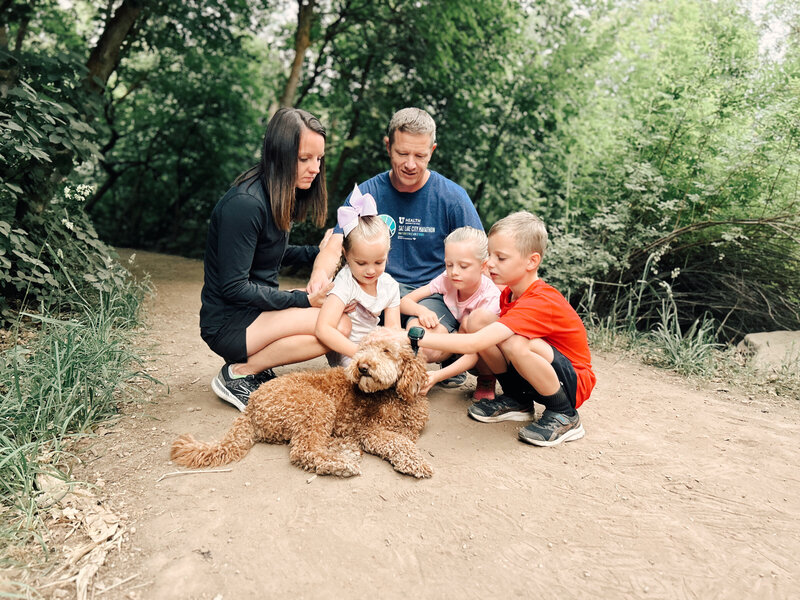 A married couple and their three children petting the golden doodle puppy while on a hiking trail | Cornerstone Dog Training