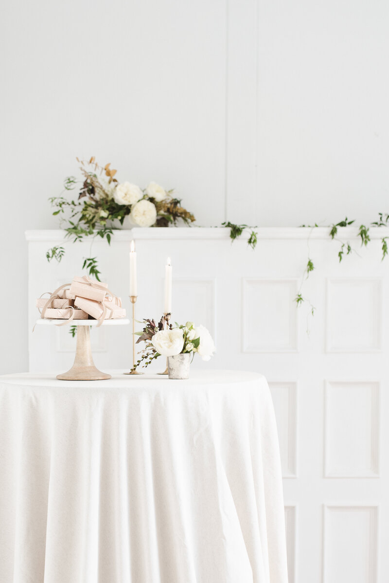 Tiny Gifts on a gold cake stand next to a white floral centerpiece. 