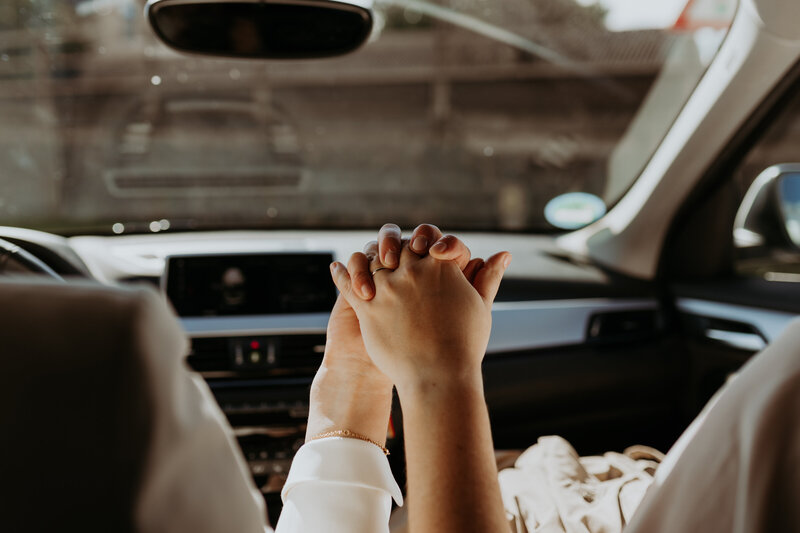 Hochzeitspaar hält Hände im Auto 