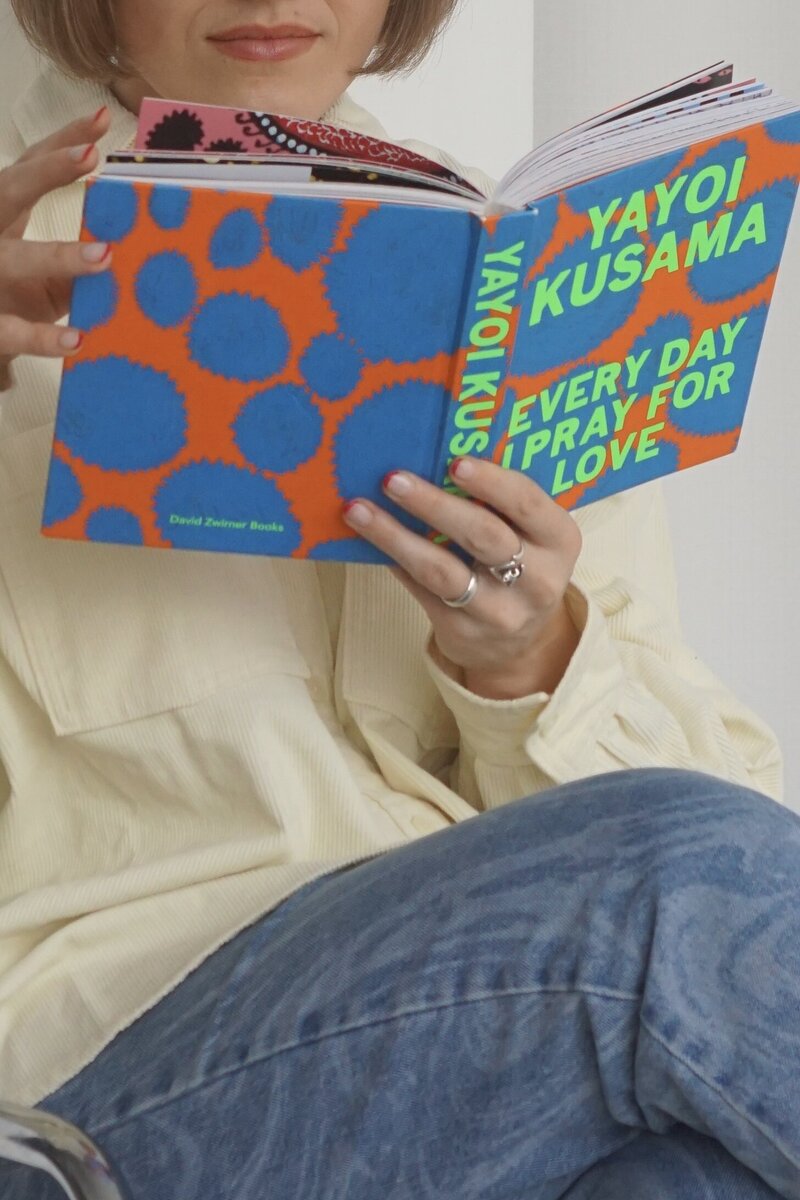 Two hands are looking through a bright orange and blue book. In neon green, the titple says "Every day I pray for love"