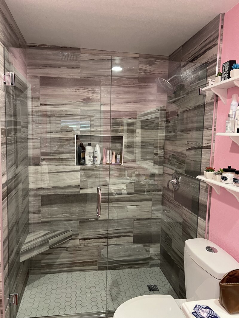 A shower with dark and light grey faux wood tiles and a new glass shower door and hardware.