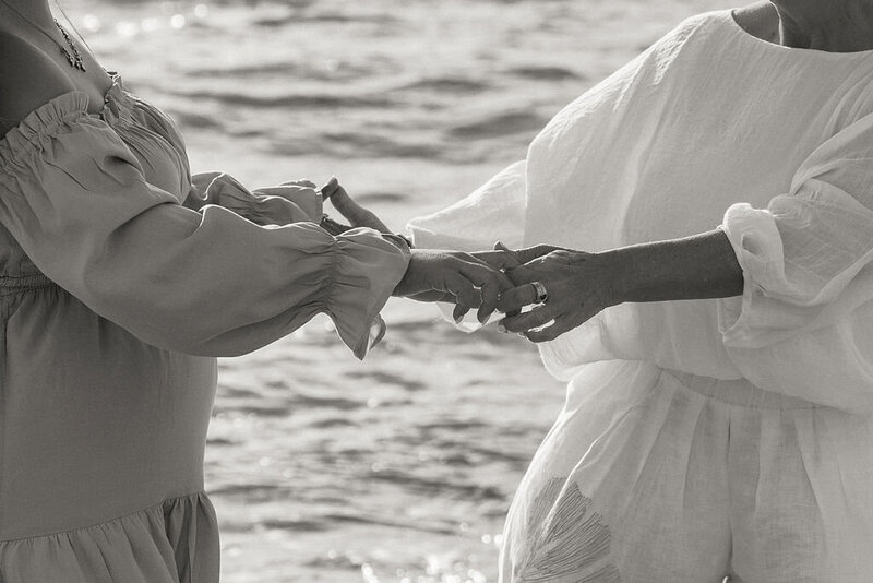 Black and white photo of pregnant woman and elder holding hands at Miami beach maternity session, symbolizing generational connection.