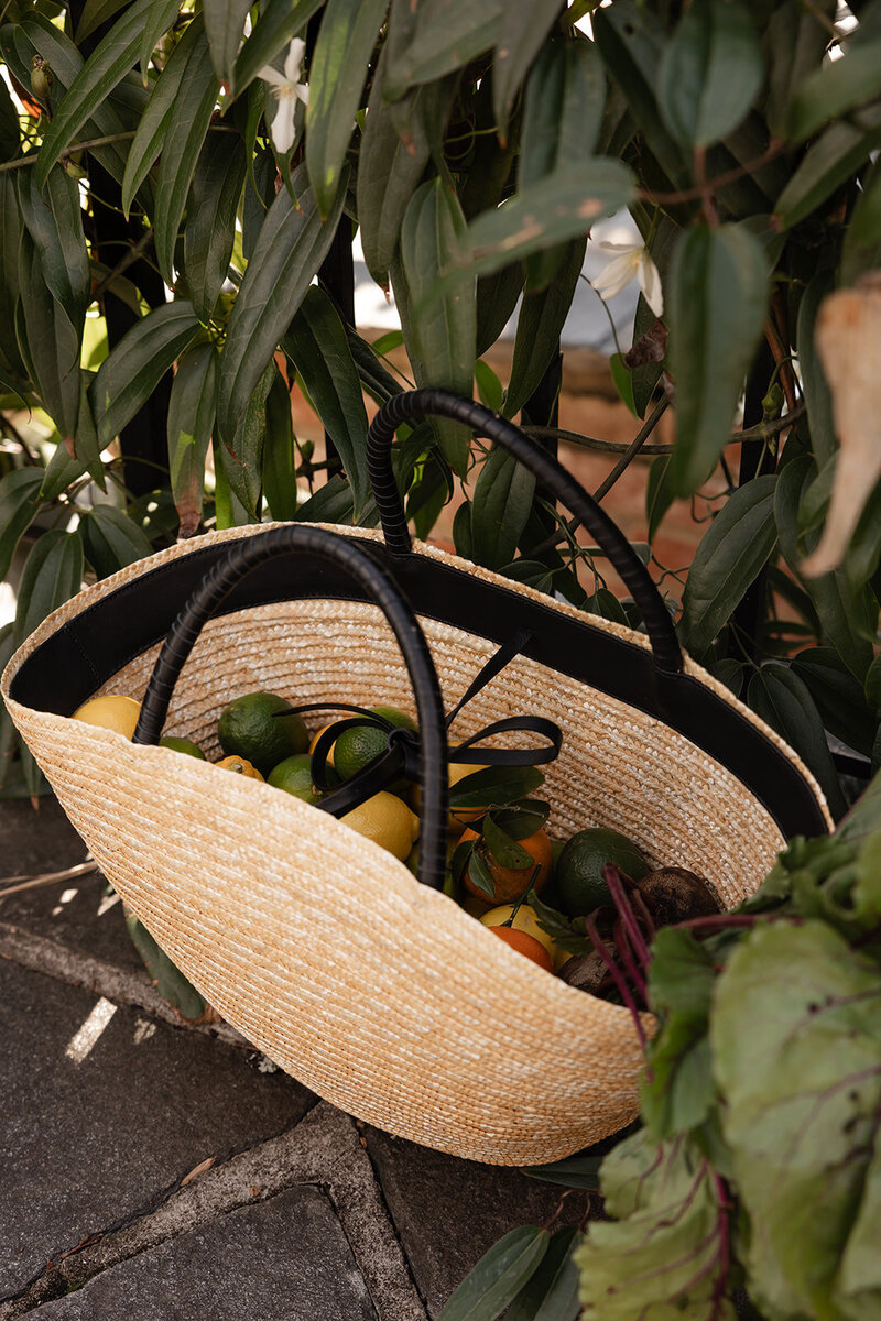 A colorful basket of seasonal fruits and vegetables resting on the ground, symbolizing nourishing, whole-food living