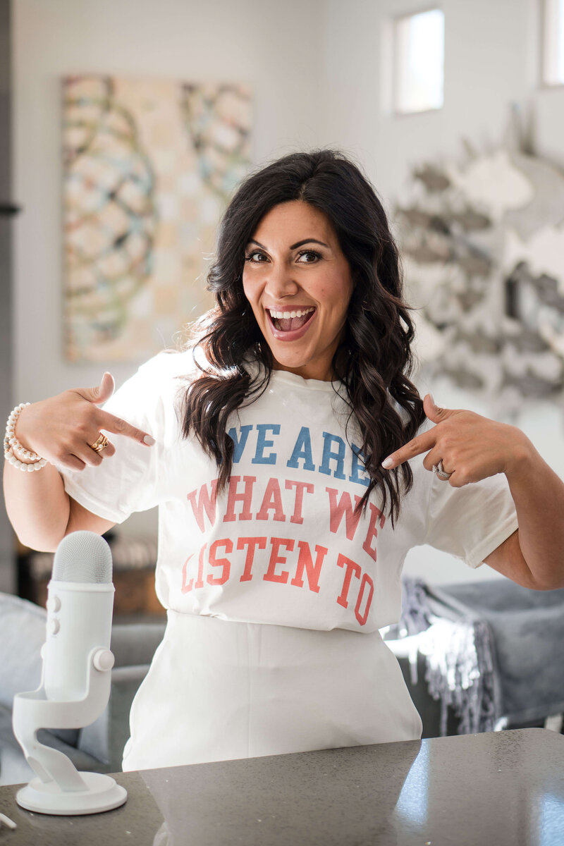 woman with short dark haor wearing a yellow floral shirt and bright lipstick laughing with iced coffee and blue yeti microphone in front of her