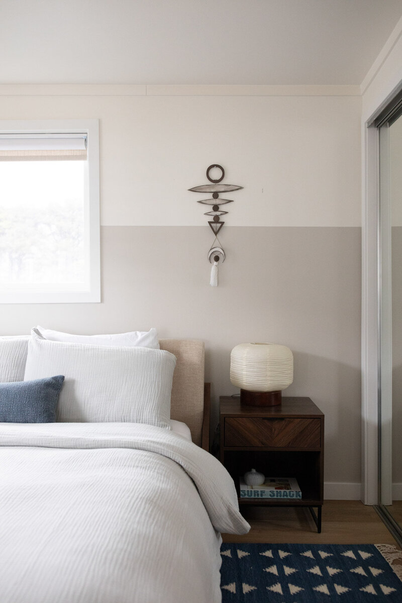 A bed and painted wall with artwork, representing eclectic home decor in a short term rental designed by Winsome Home Interiors.