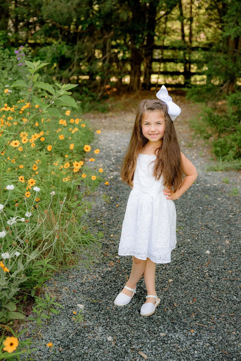 little waxhaw girl poses with her hand on her hip wearing a white dress and bow