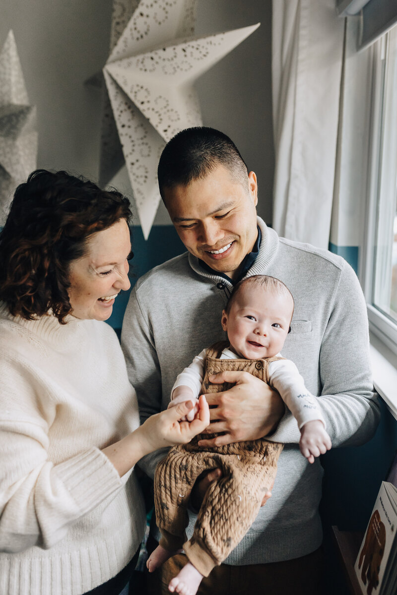Family cuddles together on bed as toddler laughs