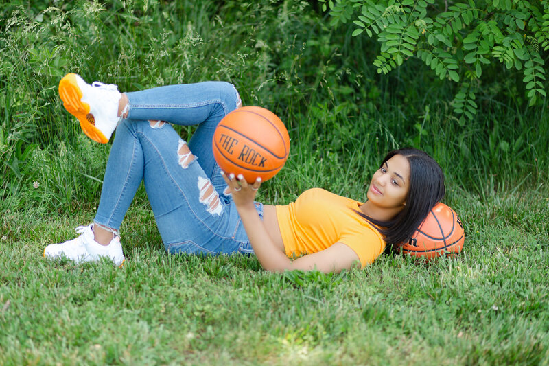 Female basketball player laying on a basketball and holding one in her left hand