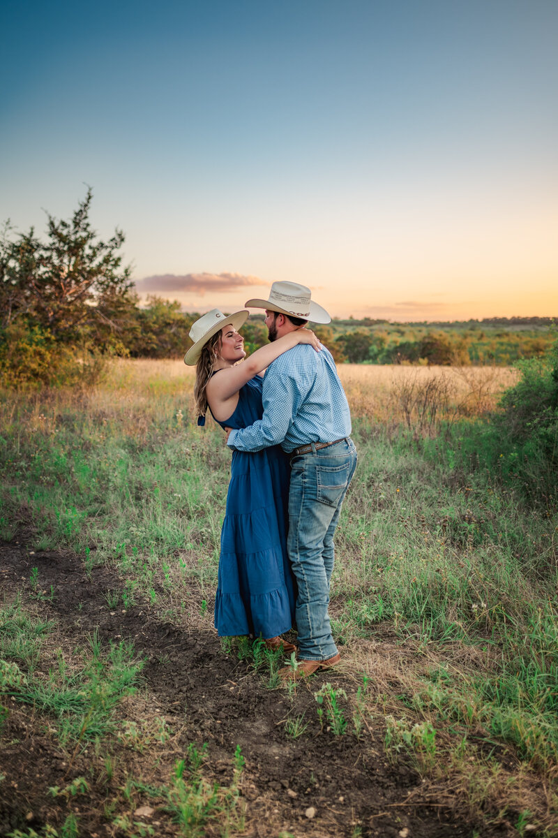 Engaged couple embracing at sunset in the Texas Hill Country during lifestyle engagement session.