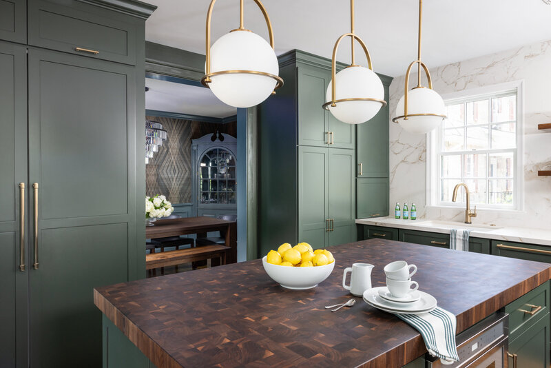 foxhall green full height cabinetry and island with walnut butcher block counter top, globe and glass pendant lights, brass faucet, window, marble-look white quartz counter top and full-height backsplash