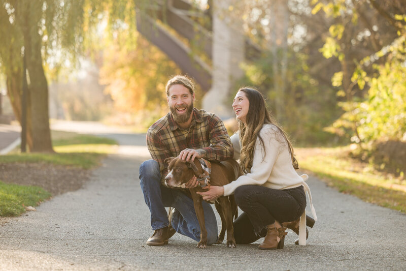 Couple walking along a scenic path with their dog in Phoenixville, capturing an outdoor moment during their engagement session.