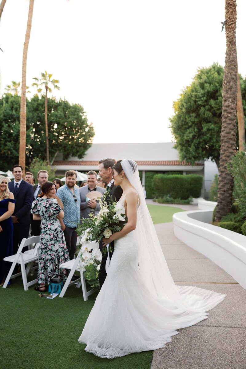 Father walks bride down the aisle at the Scott Resort in Scottsdale and guests smile.