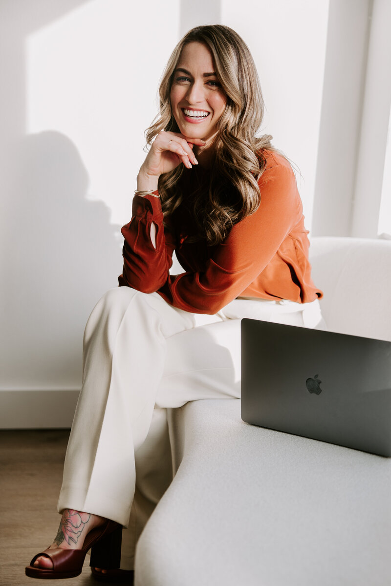 Portrait of SEO website copywriter Erika Fitzgerald sitting on a white sofa