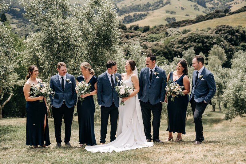 bridal party in navy and grey stand in olive trees in akaroa at mt vernon lodge photo spot