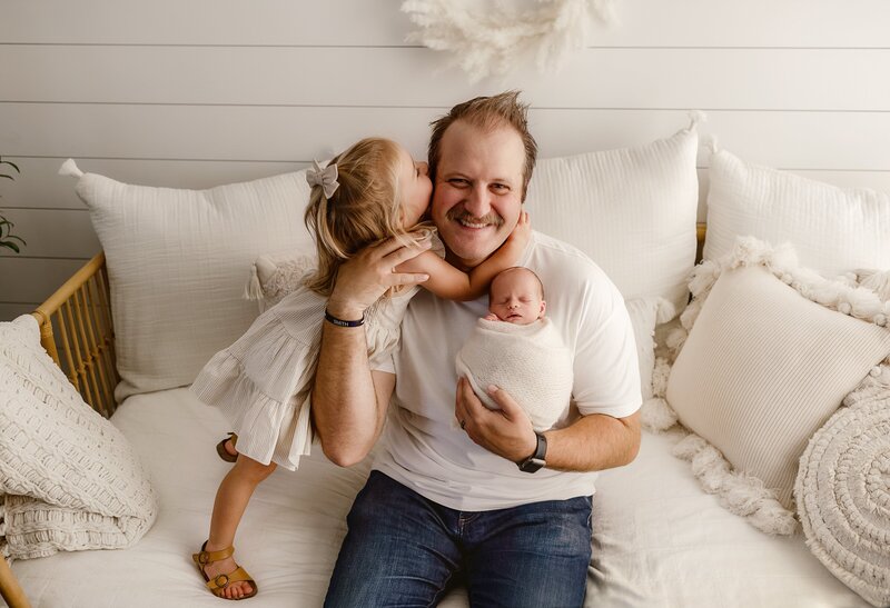 dad holds brand new baby boy while his daughter gives him a kiss during their newborn pictures in denver studio