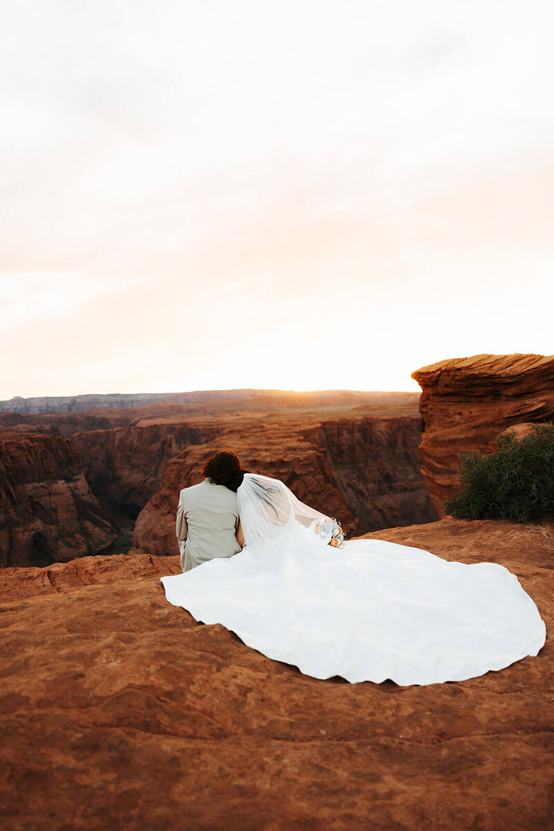 Bride and groom sit on cliff overlooking canyon