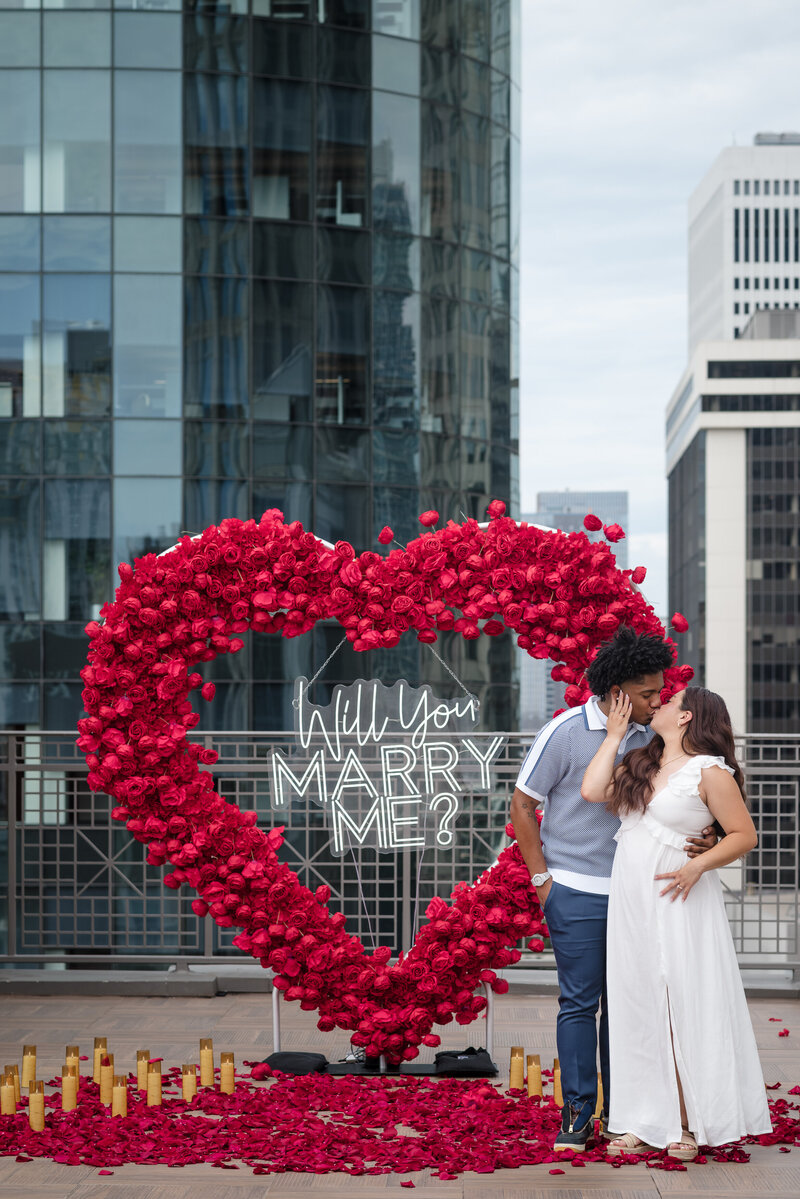 Romantic Uptown Charlotte proposal setup with red roses, candles, and skyline view, photographed by proposal photographer in Charlotte.