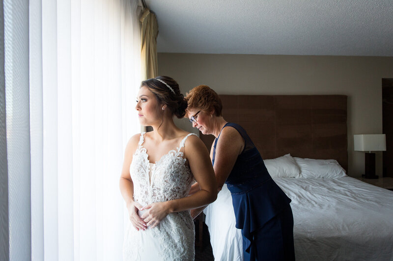 mother of the bride buttoning up bride's dress on morning of wedding day