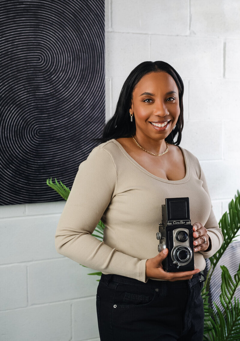 Kesha Wright holding a camera, smiling during a behind-the-scenes branding session.