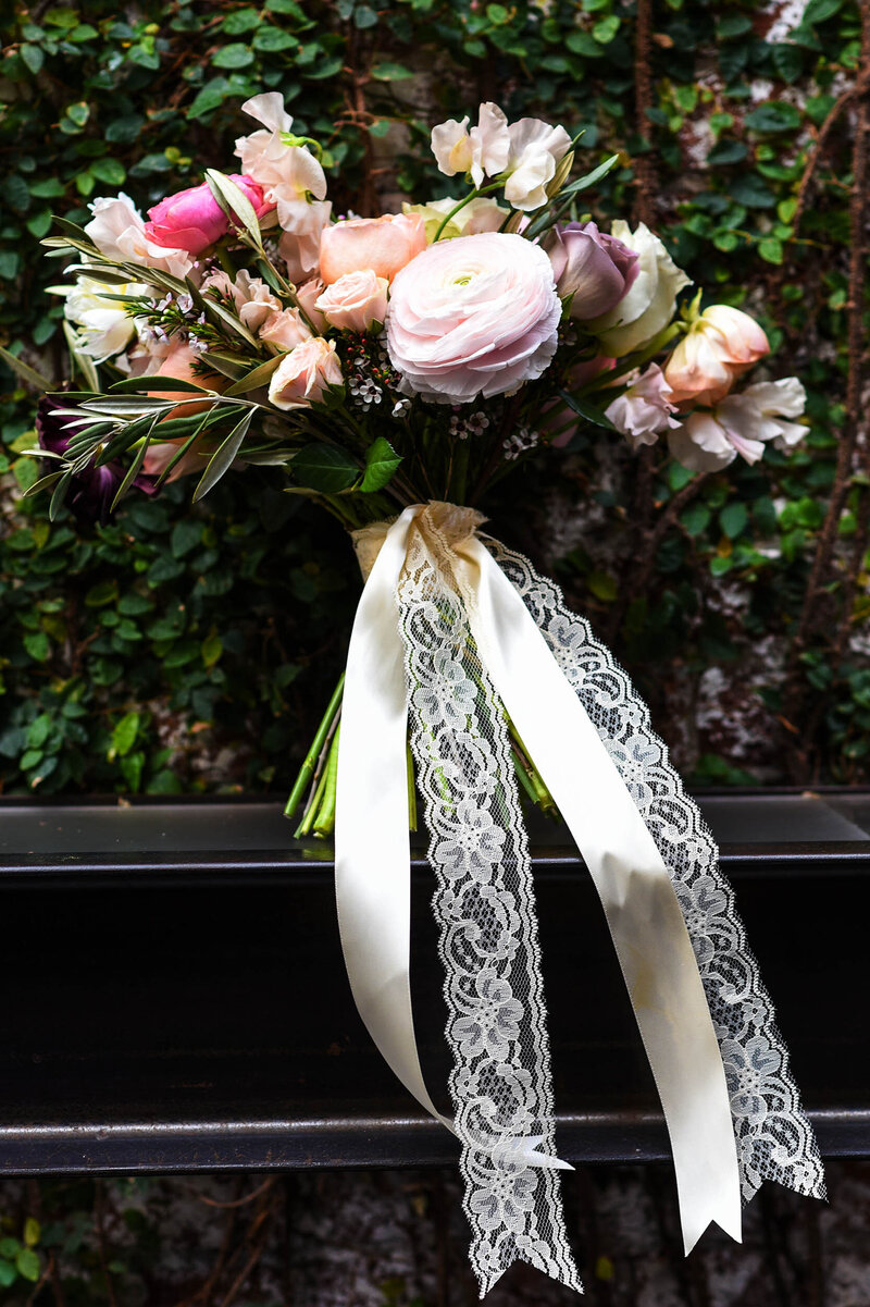 Whimsical bridal boquet bound with lace and satin ribbons sitting on iron rod in the greenery of The Foundry.