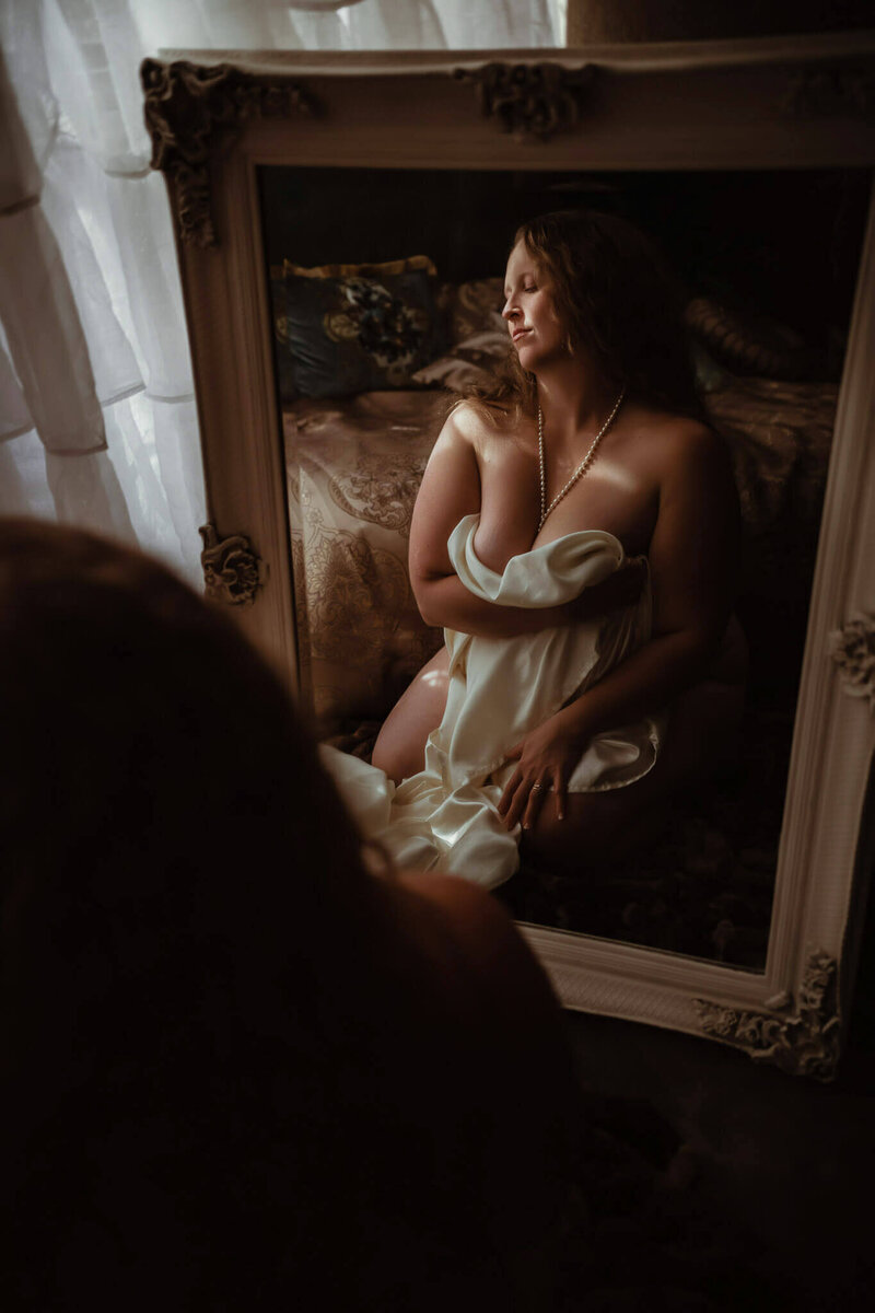 Woman with blond curly hair facing a mirror during boudoir photography session.