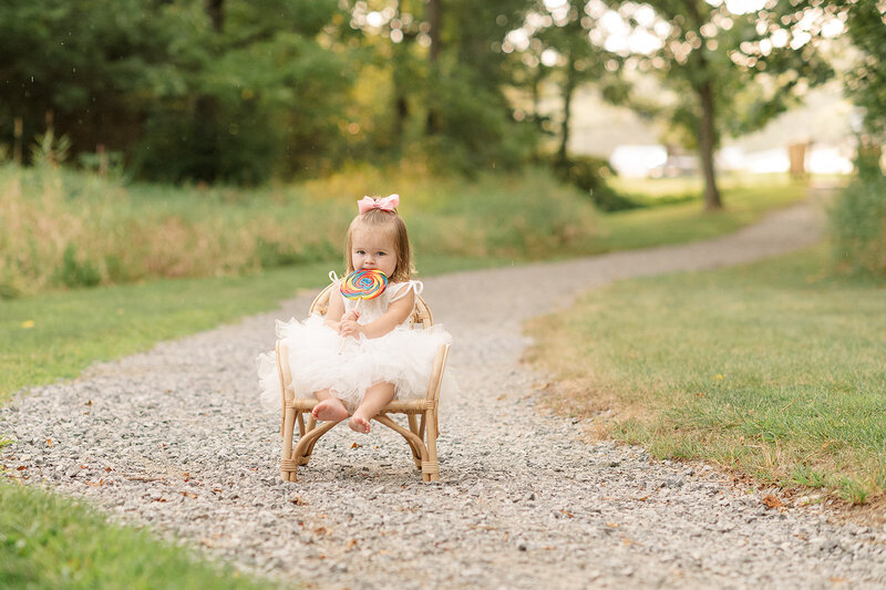 little girl sitting on a chair on a stone path with a lollypop by york pa photographer