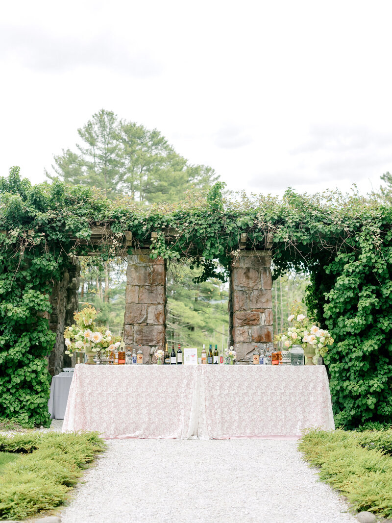 Pink and green cocktail hour bar with hosted liquor bottles on the bar at a destination New England wedding in the Berkshires.